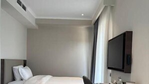 Habitación de hotel con cama, escritorio, silla, televisión y piso alfombrado.