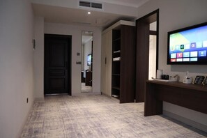 A hotel hallway with a carpeted floor, a dark wooden door, a mirror, a wardrobe, and a flat-screen TV mounted on the wall.