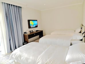 Habitación de hotel con dos camas, televisión, escritorio con cafetera y ventana con cortinas.