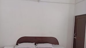 A single bed with a wooden frame and white bedding, a ceiling fan, and a closed door.