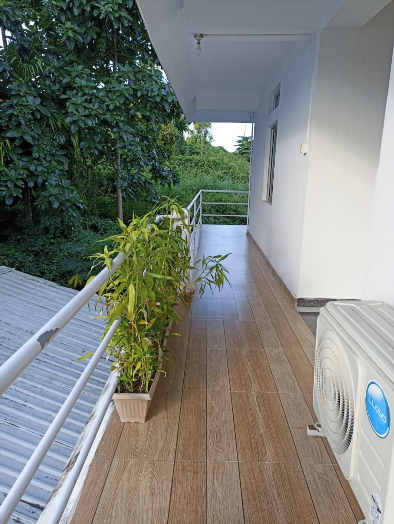 A balcony with a wooden floor, a white railing, and a white air conditioning unit.