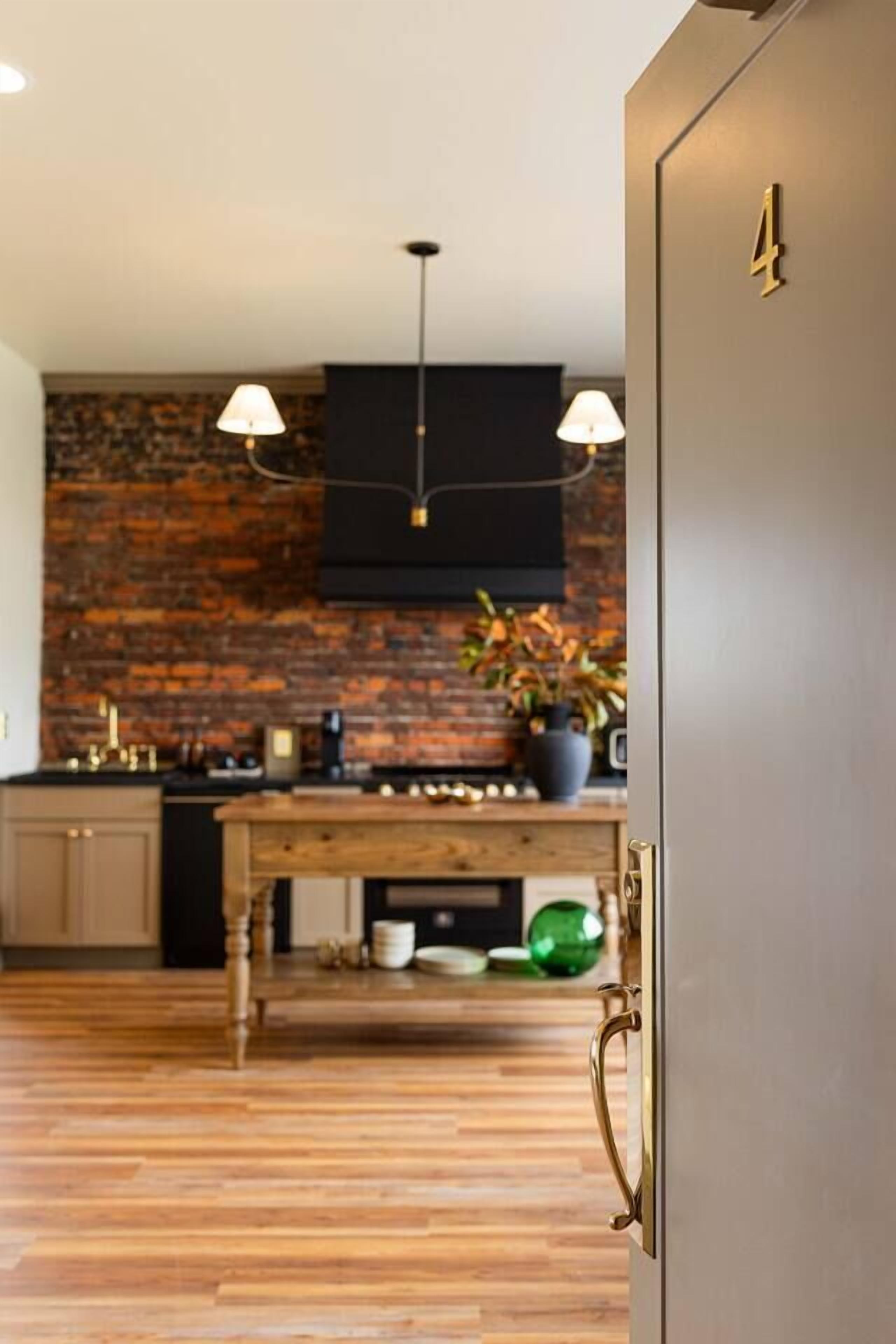 A modern kitchen with a brick wall, wooden flooring, and a black range hood.