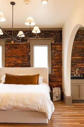 Ein Schlafzimmer mit Backsteinwand, einem Bett mit weißer Bettwäsche und einer Kristallleuchter.