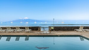 Una piscina amb gandules orientades cap a una vista al mar, una paret de pedra i un senyal de precaució.