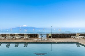 Ein Pool mit Liegestühlen, Blick auf das Meer, eine Steinmauer und ein Warnschild.