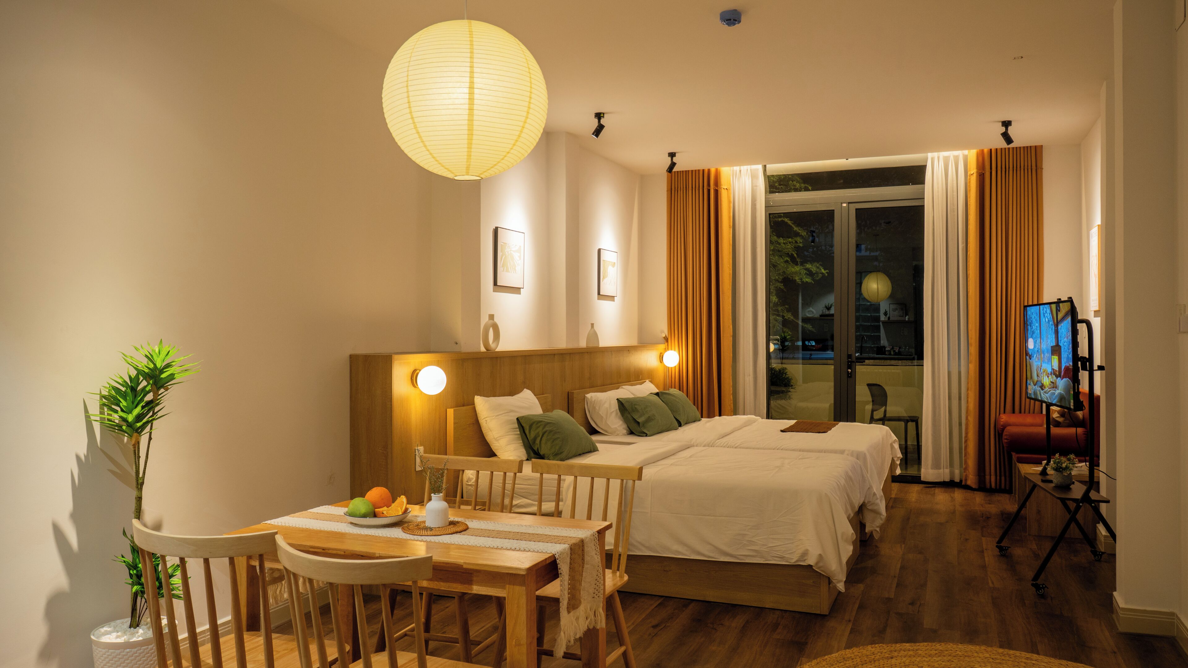 Ein Hotelzimmer mit Bett, Schreibtisch mit Stuhl, Esstisch, Fernseher und Blick ins Freie.