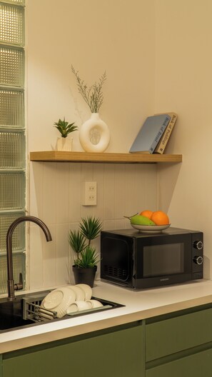 A kitchen with a microwave, a fruit bowl, a potted plant, and a book on a shelf. - Near Ben Thanh Market: 2 Beds Apt by D Haus with Netflix (Thành phố Hồ Chí Minh)