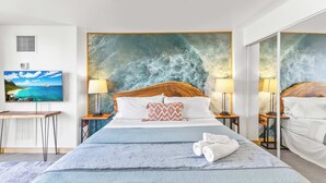 A hotel room with a large bed, two bedside tables with lamps, a large mirror, a painting of a beach, and a vent on the wall. - Modern Designer Studio in Waikiki near Ala Moana (Honolulu)