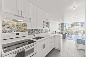 Eine moderne Küche mit weißen Schränken, einer Fliesenküchenwand und Blick auf einen Balkon mit Stadtansicht.