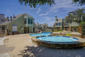 Zona residencial con piscina rodeada de muros de piedra, estacionamiento cercado y casas con chimeneas.
