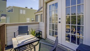 Ein kleiner Außenbereich mit Terrasse, Tisch und Stühlen, einem Blumentopf und einer Glastür, die zu einer überdachten Veranda führt.