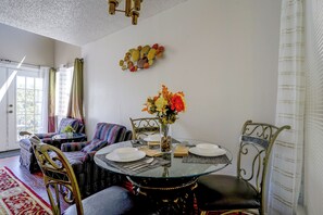 Un comedor con mesa de vidrio, sillas y un jarrón con flores.