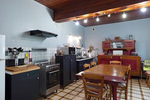 A compact kitchen with a gas stove, microwave, and a dining area with a wooden table and chairs. - Gîte de Bossuet – Wi-Fi, Garden & Air Conditioning near Bordeaux & Atlantic Coast (Saint-Denis-de-Pile)