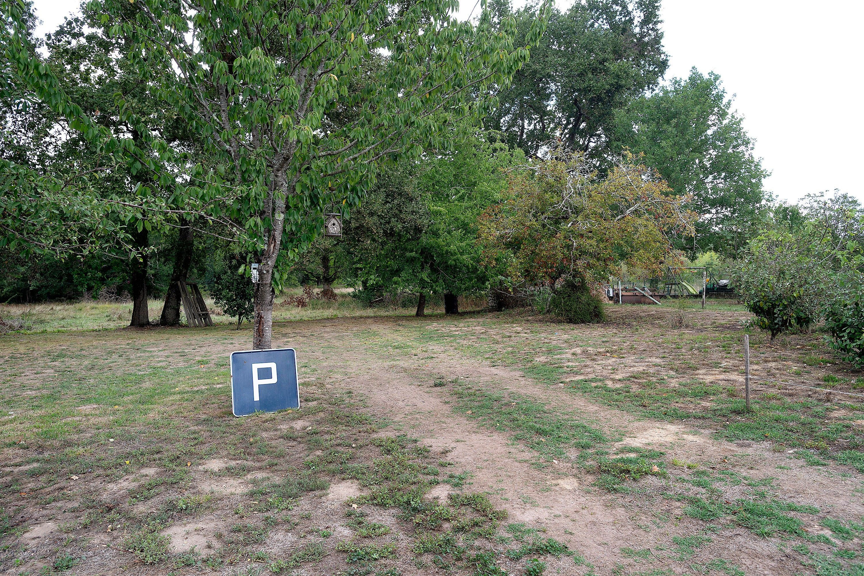 Parkschild in einer grünen Umgebung mit Bäumen und einem Feldweg.