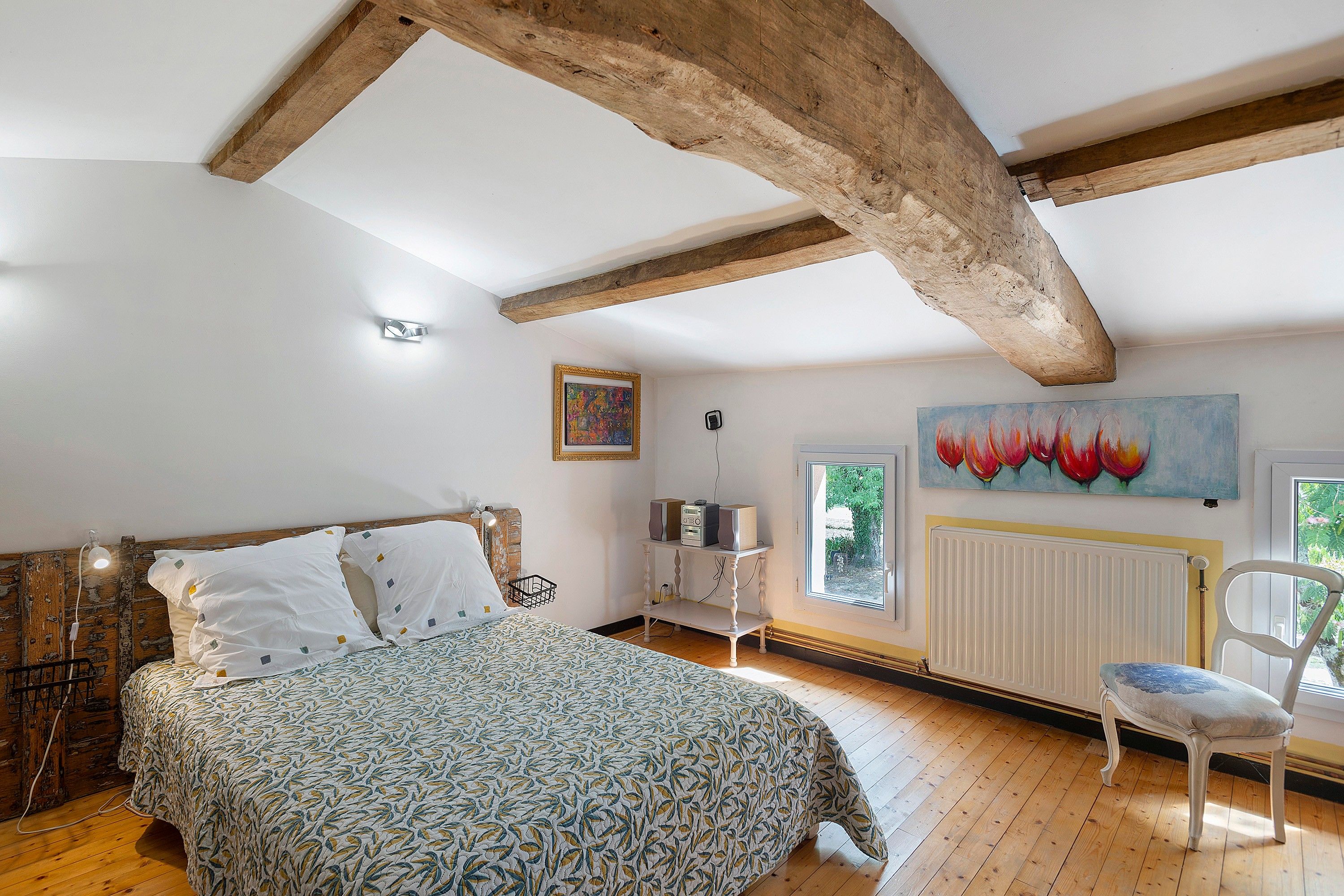 Ein Schlafzimmer mit einem Bett, einem Sessel, einer Heizung, einem Fenster und Bildern an der Wand.