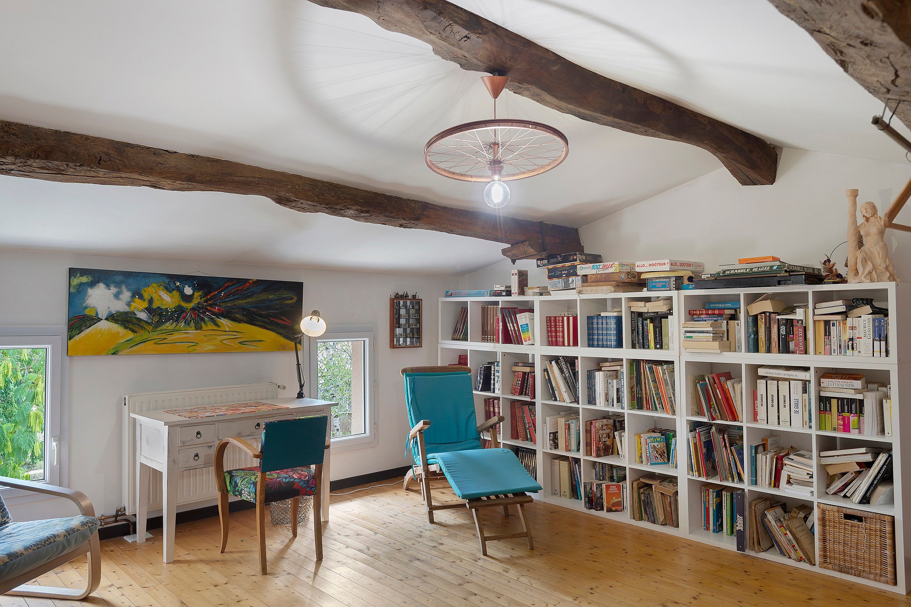Una habitación con techo de madera, una estantería llena de libros, un escritorio con una silla y un cuadro en la pared.