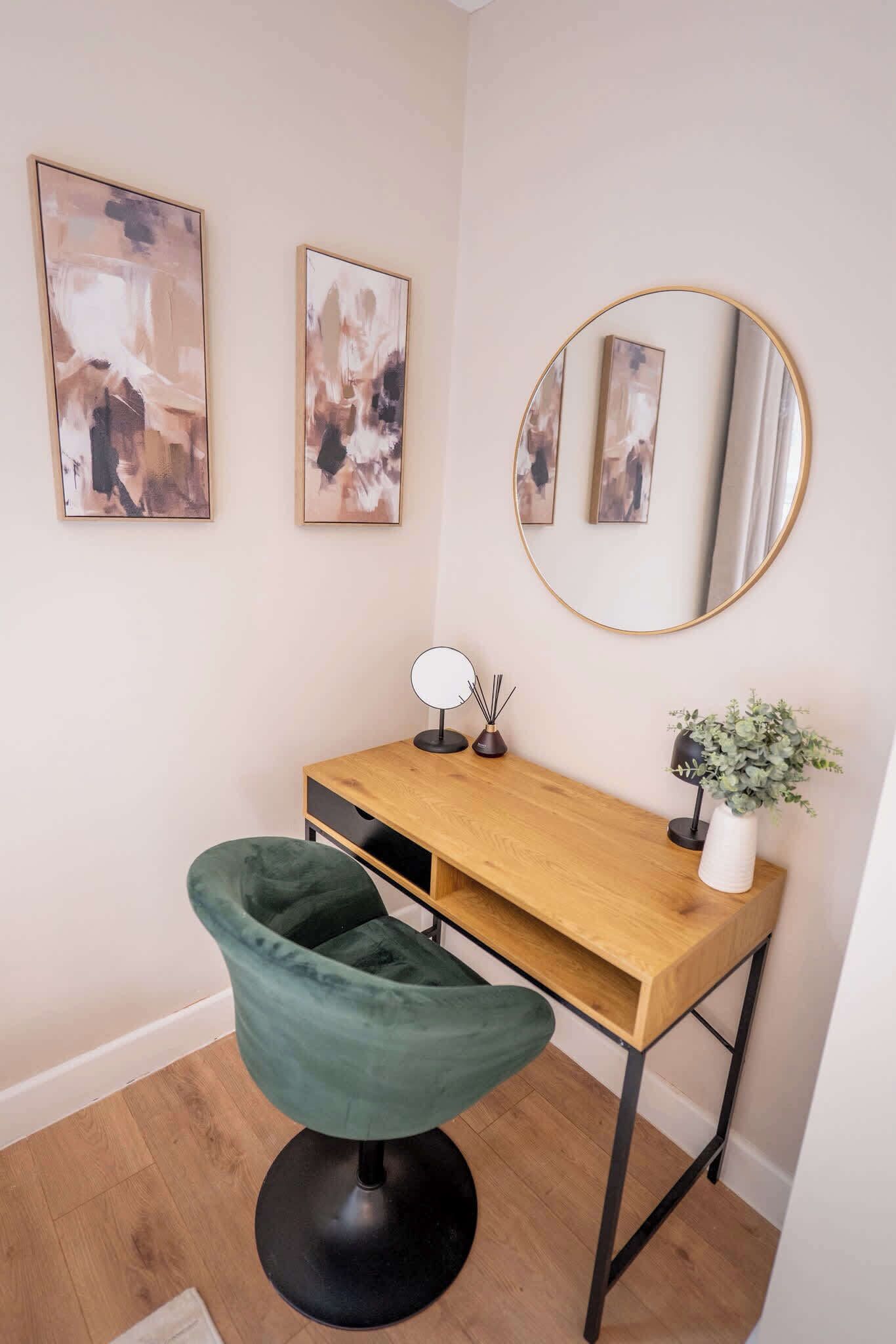 A modern workspace with a wooden desk, a green chair, a round mirror, and abstract art on the wall.