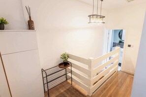 A modern interior with a wooden floor, white walls, a metal rack, and a hanging light fixture.