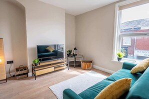 A living room with a television, a sofa, a coffee table, and a window with a view of a building.