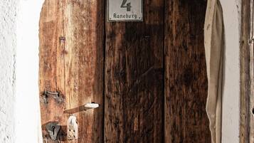 Eine rustikale Holztür mit einem Schild darüber, ein Metallgitter mit Kette und eine weiße Mauer.