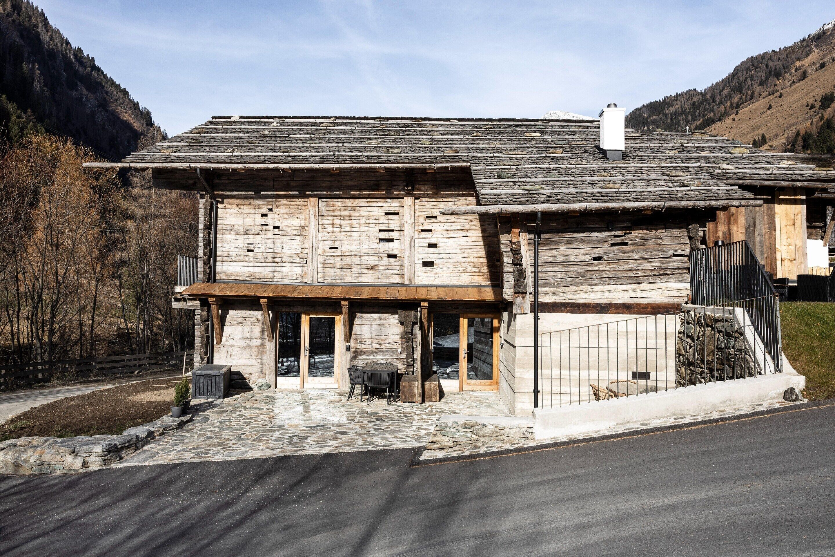 Ein rustikales Holzgebäude mit Steinunterbau, einer Holzveranda und einer Steintreppe, die zum Eingang führt.