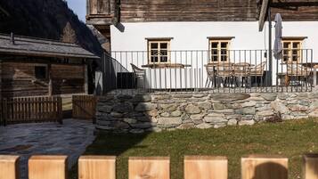 A traditional chalet with a stone wall, wooden fence, and outdoor seating area.