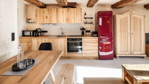 A kitchen with wooden cabinets, a red refrigerator, a built-in oven, and a dining area with a wooden table. - Elegant Apartment in a Converted Stable (Matrei in Osttirol)