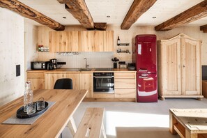 A kitchen with wooden cabinets, a red refrigerator, a built-in oven, and a dining area with a wooden table. - Elegant Apartment in a Converted Stable (Matrei in Osttirol)