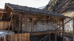 A rustic wooden cabin with a steep roof, surrounded by snow and mountains. - Elegant Apartment in a Converted Stable (Matrei in Osttirol)