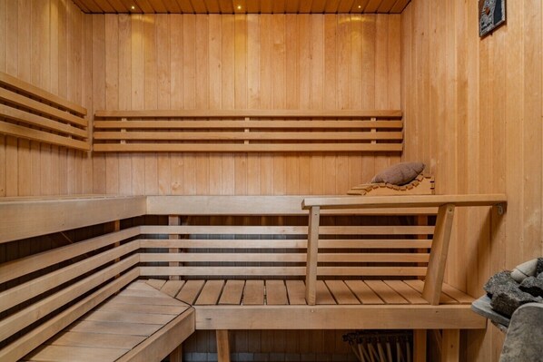 A wooden sauna with benches and a table, a towel, and a stone feature.
