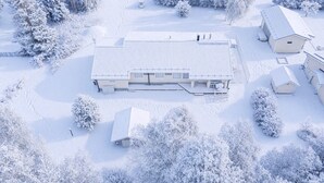 A snow-covered building with a flat roof, surrounded by snow-laden trees and a clear sky.