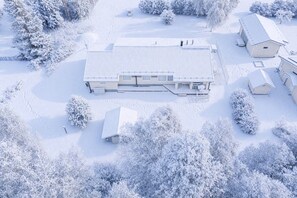 A snow-covered building with a flat roof, surrounded by snow-laden trees and a clear sky.