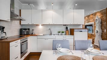 Une cuisine moderne avec des meubles blancs, un coin repas avec une table dressée pour deux personnes et une horloge décorative au mur.