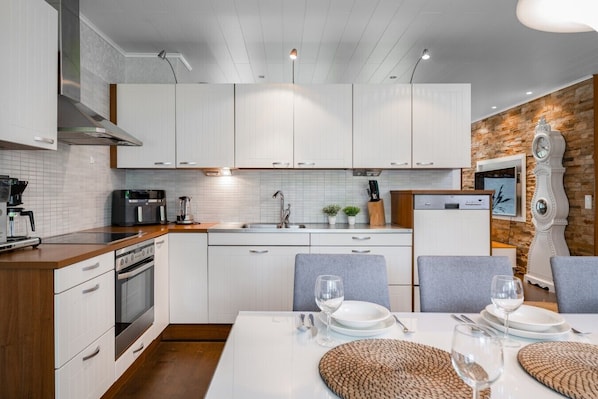 A modern kitchen with white cabinetry, a dining area with a table set for two, and a decorative clock on the wall.
