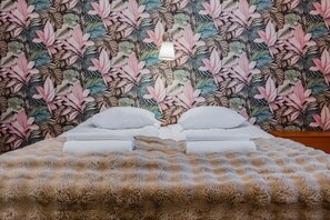 A bed with a fluffy blanket, white pillows, and a tropical leaf pattern wallpaper.