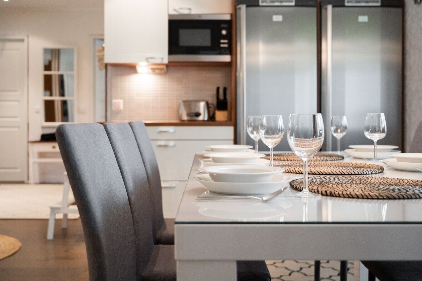 A modern kitchen with a dining table set for four, including wine glasses and plates.