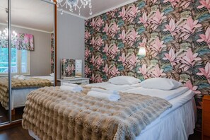 A bedroom with a large mirror, a bed with a fluffy blanket, a nightstand, and a wall with a tropical leaf pattern. - Villa Korpieukko, Private Sauna By Lapland Host (Rovaniemi)