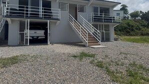 A two-story building with a car parked in the driveway, a staircase leading to the upper level, and a clear sky. - Rico Puerto magic spot oeste (Cabrera)