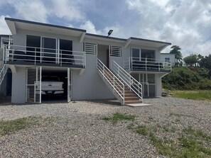 A two-story building with a car parked in the driveway, a staircase leading to the upper level, and a clear sky. - Rico Puerto magic spot oeste (Cabrera)