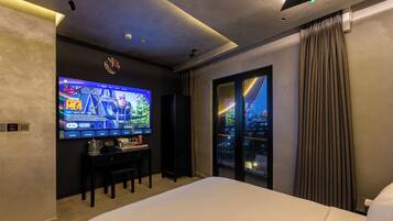 A hotel room with a large flat-screen TV displaying a movie, a bed, a coffee table with snacks, and a view of a cityscape through a glass door.