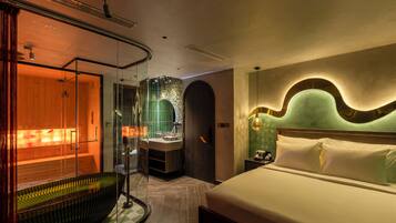 Ein modernes Hotelzimmer mit einem großen Bett, einer in Glas eingefassten Sauna und einem separaten Badezimmer mit smaragdgrüner Fliesenwand.