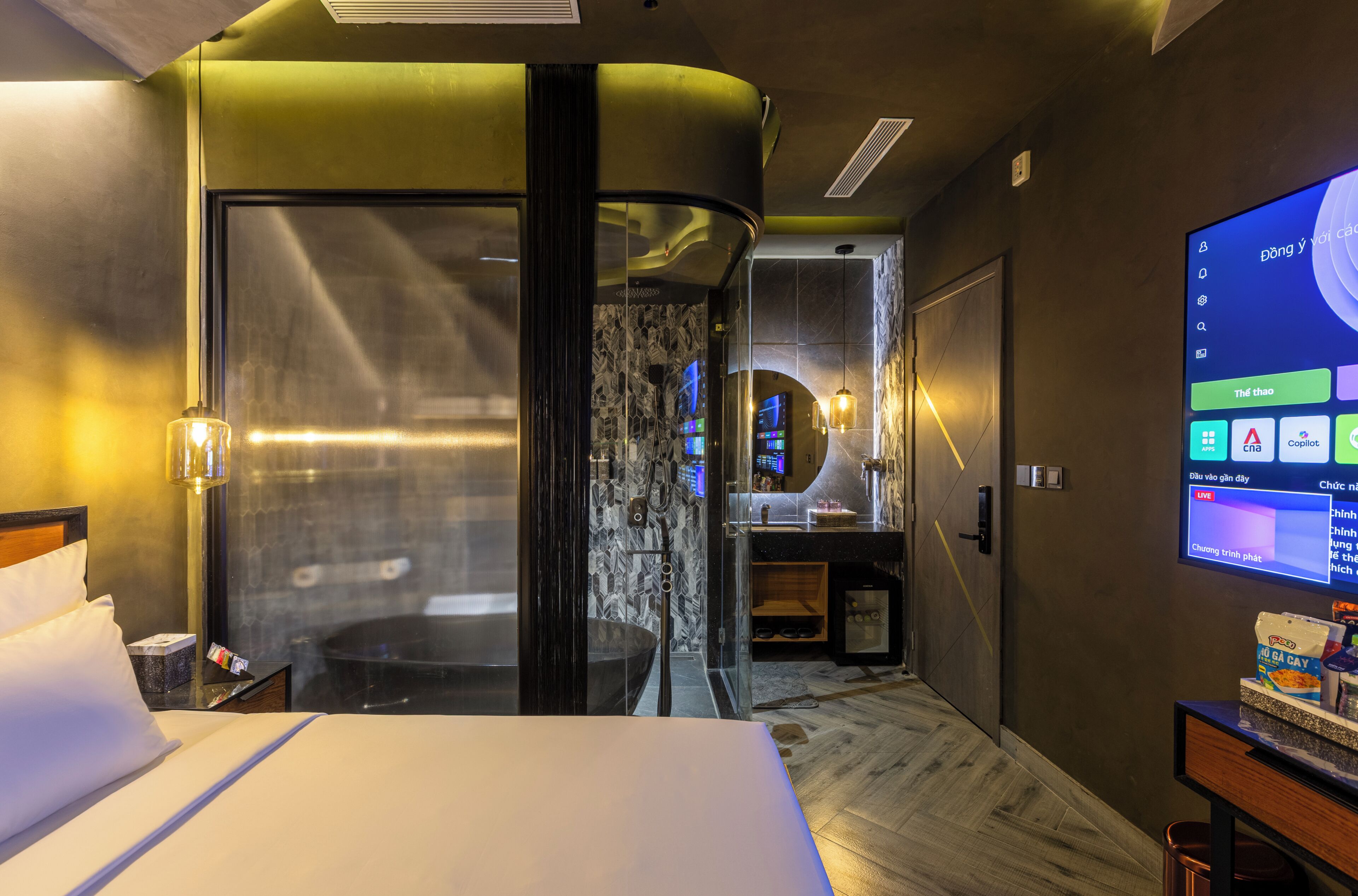 A hotel room with a bed, a desk with a computer, a TV, and a bathroom with a shower.