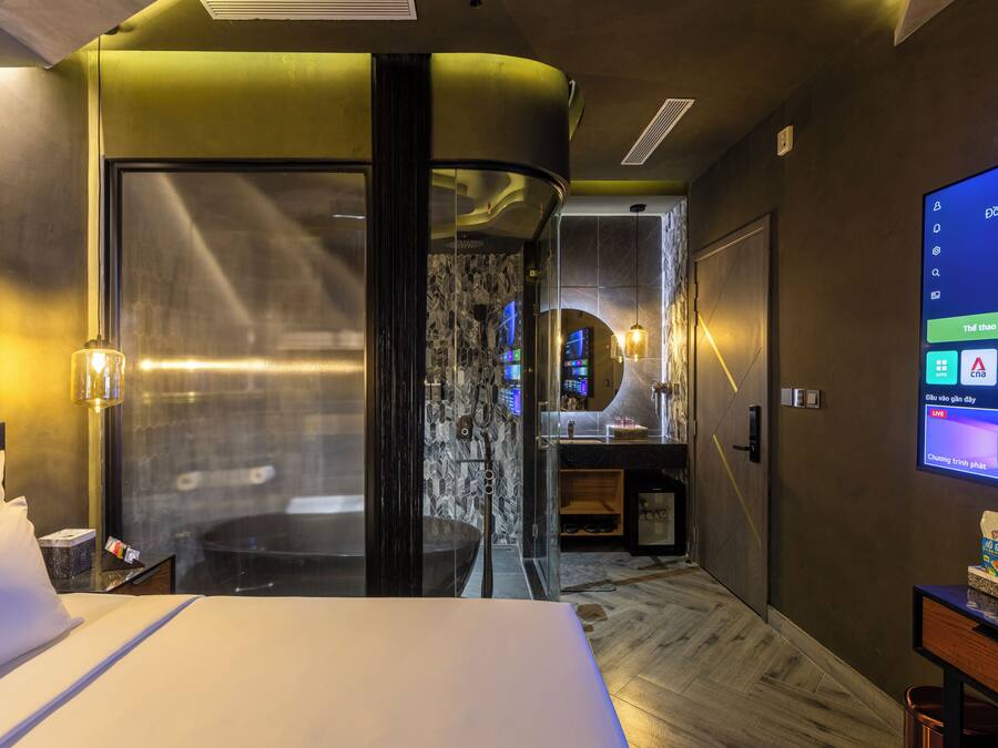 Habitación de hotel con cama, escritorio con computadora, televisor y baño con ducha.