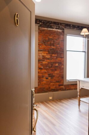 A room with a wooden floor, a brick wall, and a window.