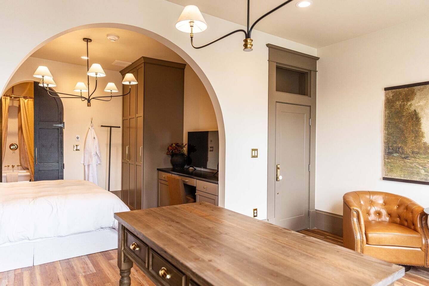 A hotel room with a bed, a wooden desk, a chair, a wardrobe, and a door.
