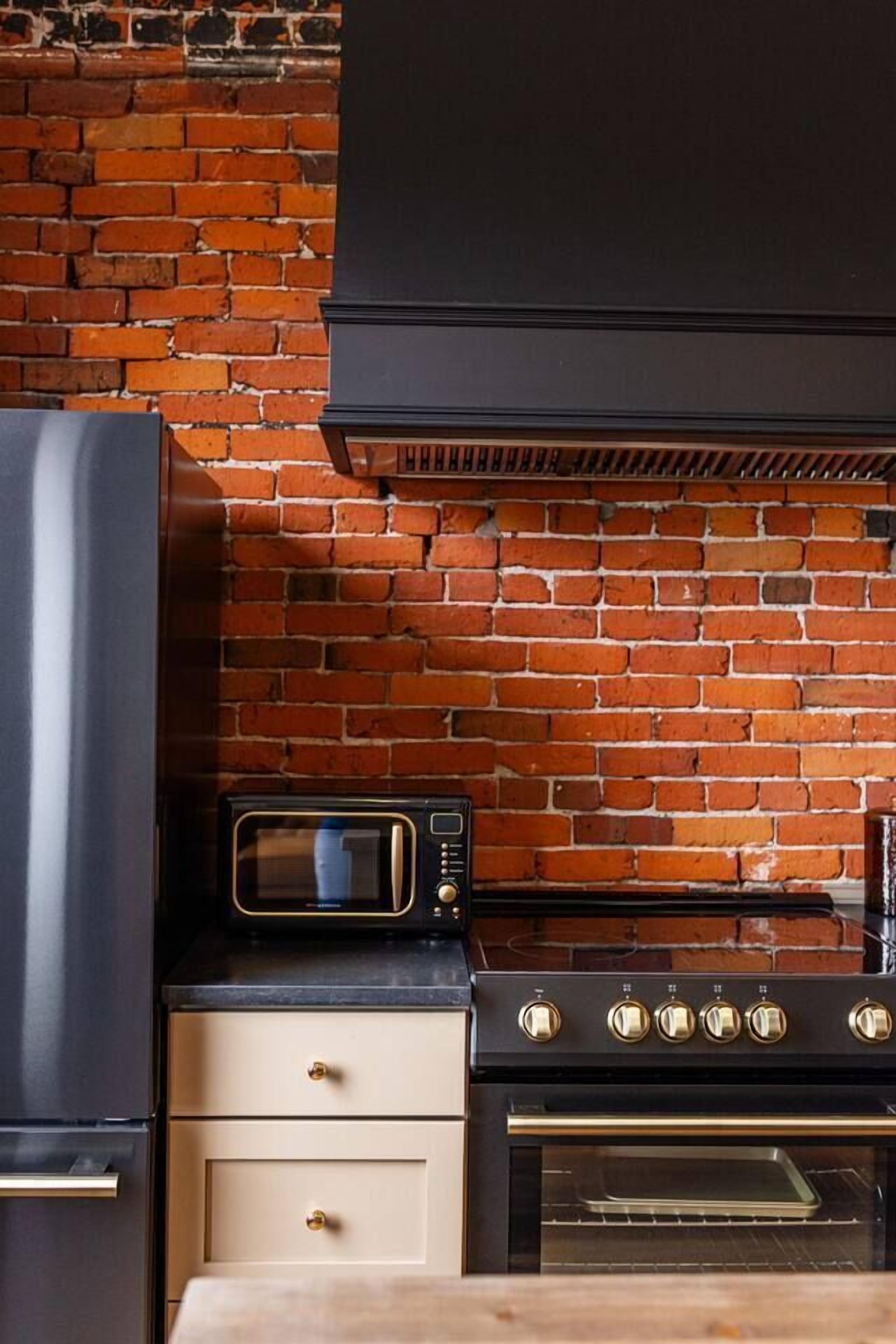 Una cocina con pared de ladrillo, microondas, estufa y refrigerador.