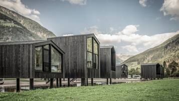 Una cabaña moderna de madera con ventanas amplias, ubicada en una zona montañosa con cielo despejado.
