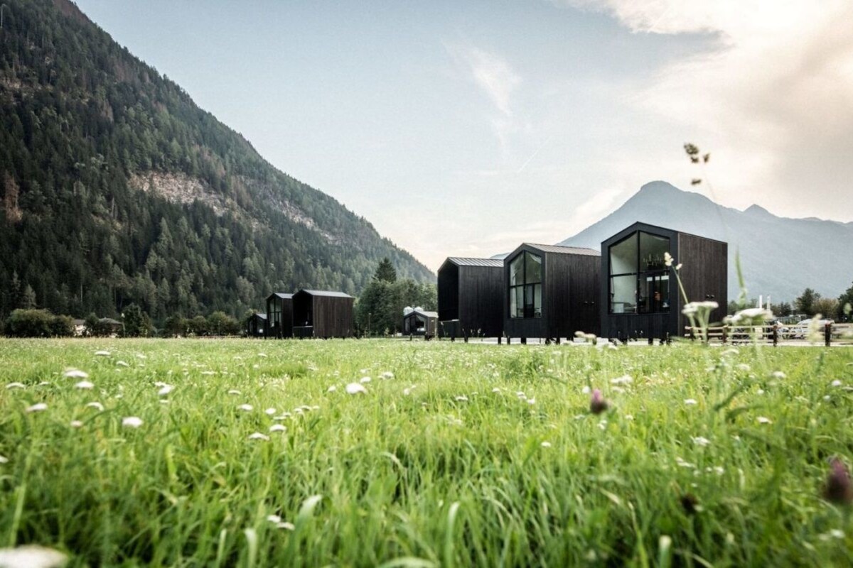 A modern building with large windows, surrounded by a grassy field and mountains in the background.