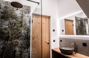 A modern bathroom with a large mirror, a wooden door, and a wall-mounted shower.