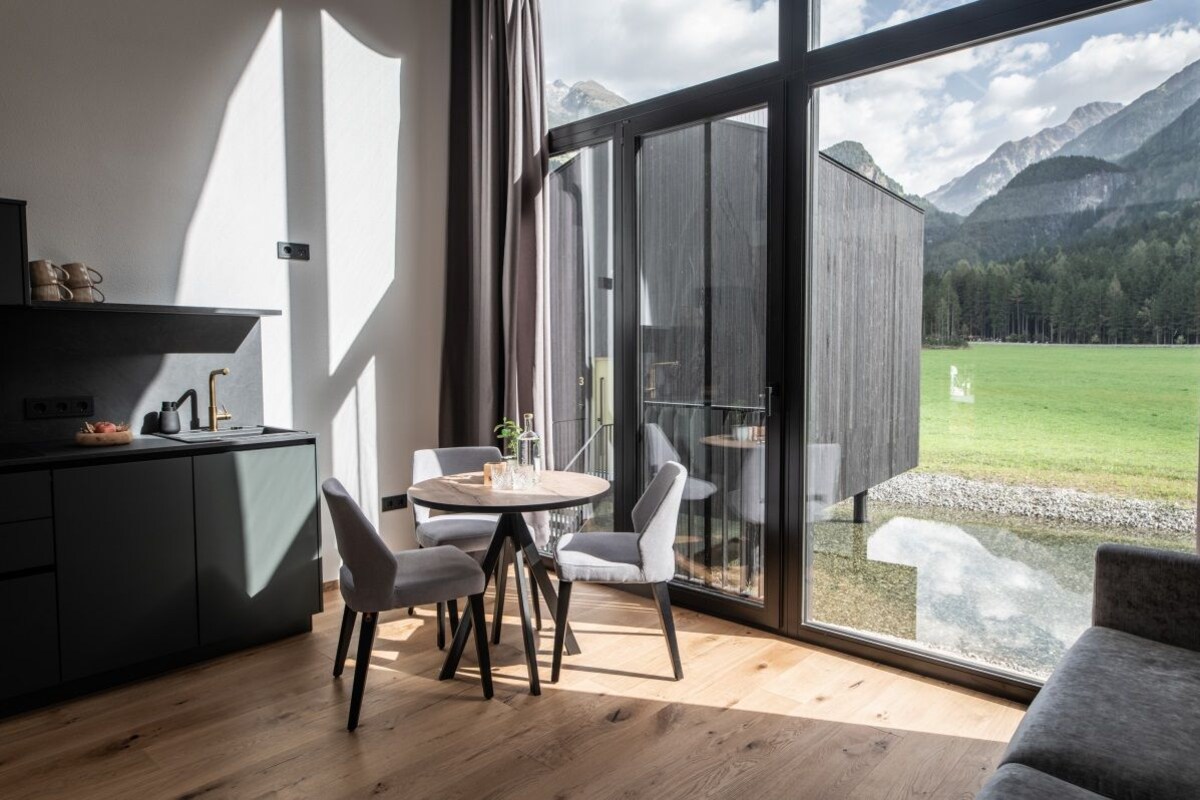 A modern interior with a dining area, a kitchen, and a large sliding glass door leading to a balcony with a mountain view.
